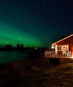 A house by the water, there are green northern lights in the sky