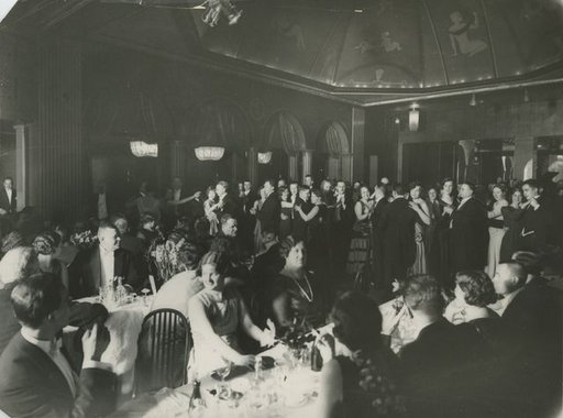 a formal party with people sitting at round tables earing and some are on the floor dancing together