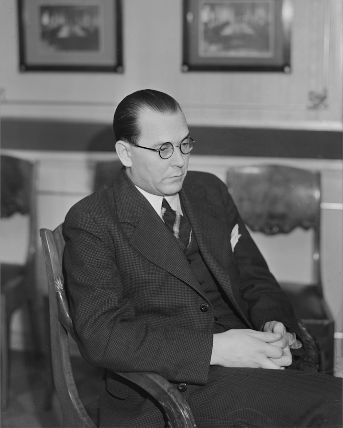 Black and white portrait of a man with glasses sitting in a chair in a suit