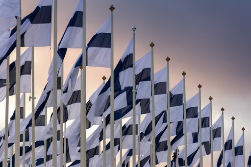 A photo of many rows of the Finnish flag in front of the sunset.