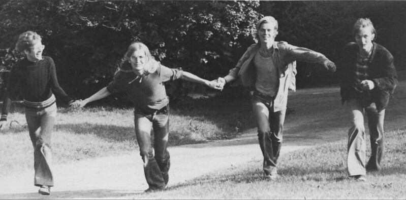 Black and white picture of people running along hand in hand with trees in the background