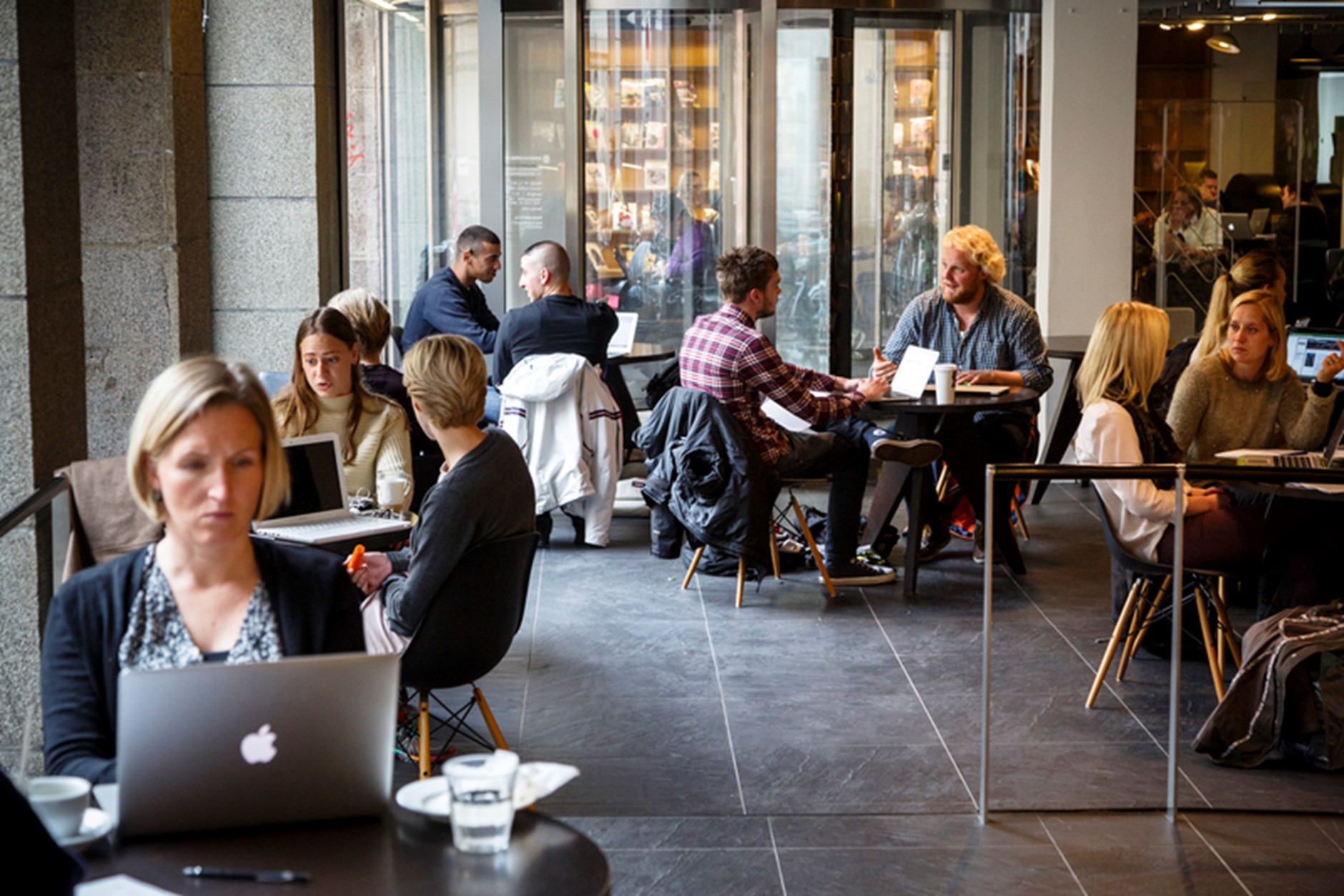 A modern looking cafe in which several people are sitting with their laptops.
