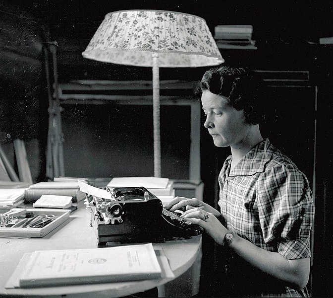 A young woman sitting by a desk writing on a typewriter