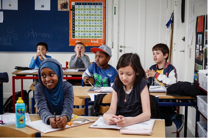 Primary school children of different ethnicities sitting in a classroom beside each other. Smiling, looking at the board.