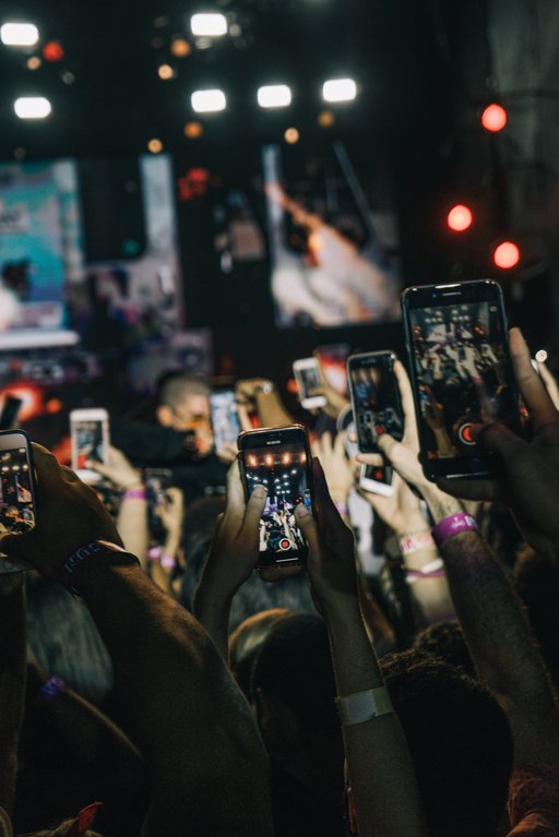 Kuva konserttiyleisön päällä olevasta älypuhelinmerestä. Jokainen yleisössä joko kuvaa videota tai ottaa kuvia. Kuva on hyvin tumma.