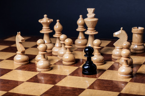 Chess board with a single black piece in the middle of all the white pieces.