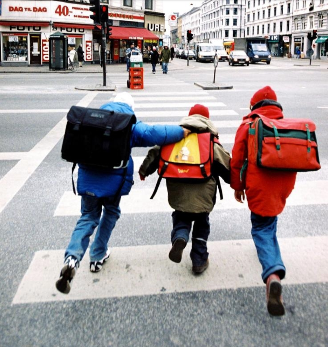 three children running across the street wearing school backpacks.