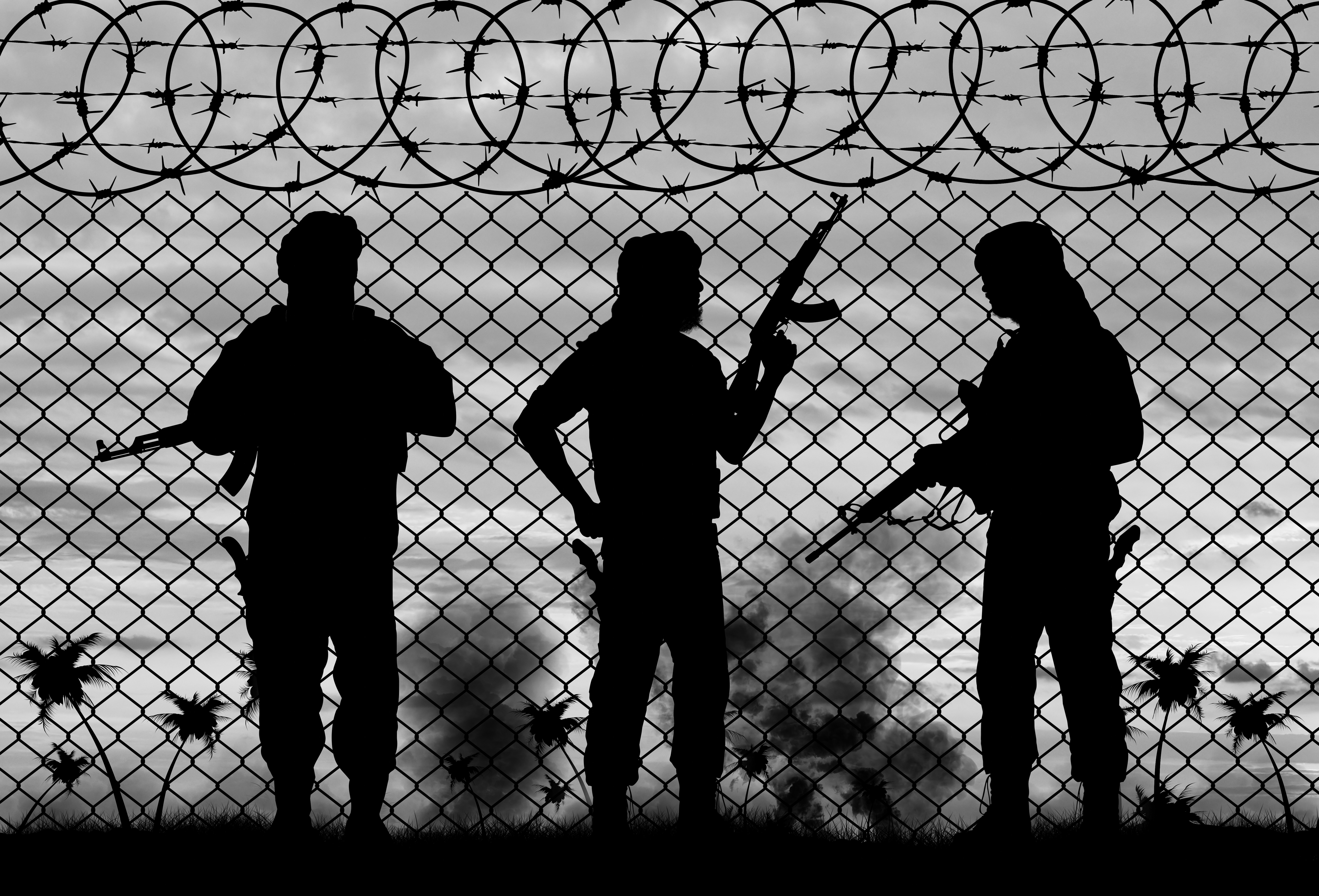 Barbed wire and the silhouette of men with guns in military clothes