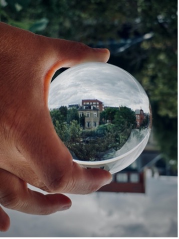 Upside down photo of a hand holding a glass ball. Through the glass ball, a green landscape and some houses are displayed, turned 180 degrees. Upside down photo of a hand holding a glass ball. Through the glass ball, a green landscape and some houses are displayed, turned 180 degrees.