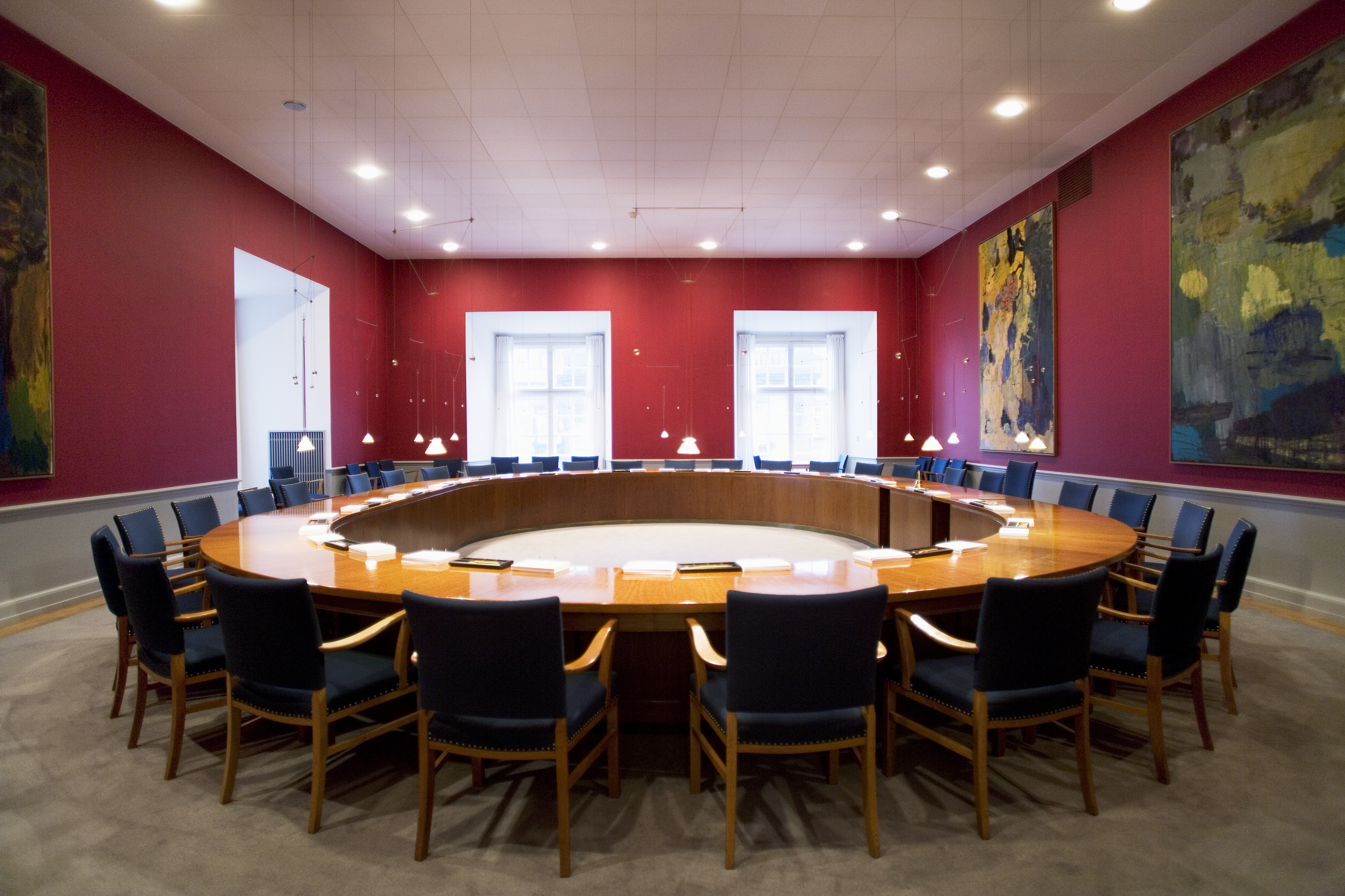 A meeting room with a large round table with chairs around it in the centre. 