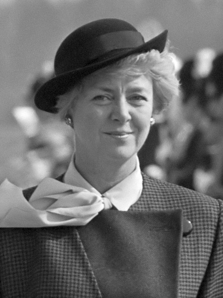 Portrait of Vigdís Finnbogadóttir. Here, she is a young woman with blond short hair, standing upright wearing a black long trenchcoat and a formal hat.