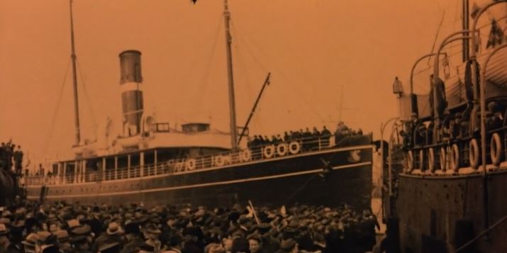 Large ship arriving at the shore with a large crowd of people cheering and waiting for them