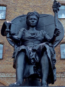 A large black statue of a woman holding two objects.